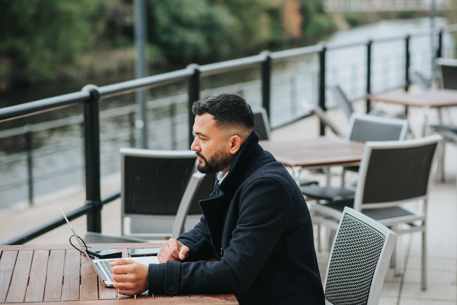 A businessman holding a laptop with a fence as the background.